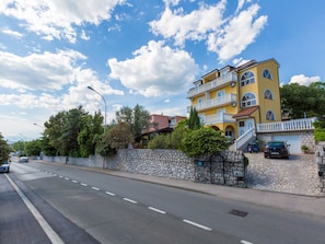A multi-story yellow building with balconies, a stone wall, and a paved road. - AKELAVA 2 / HR-05548-02 by Interhome (Crikvenica)