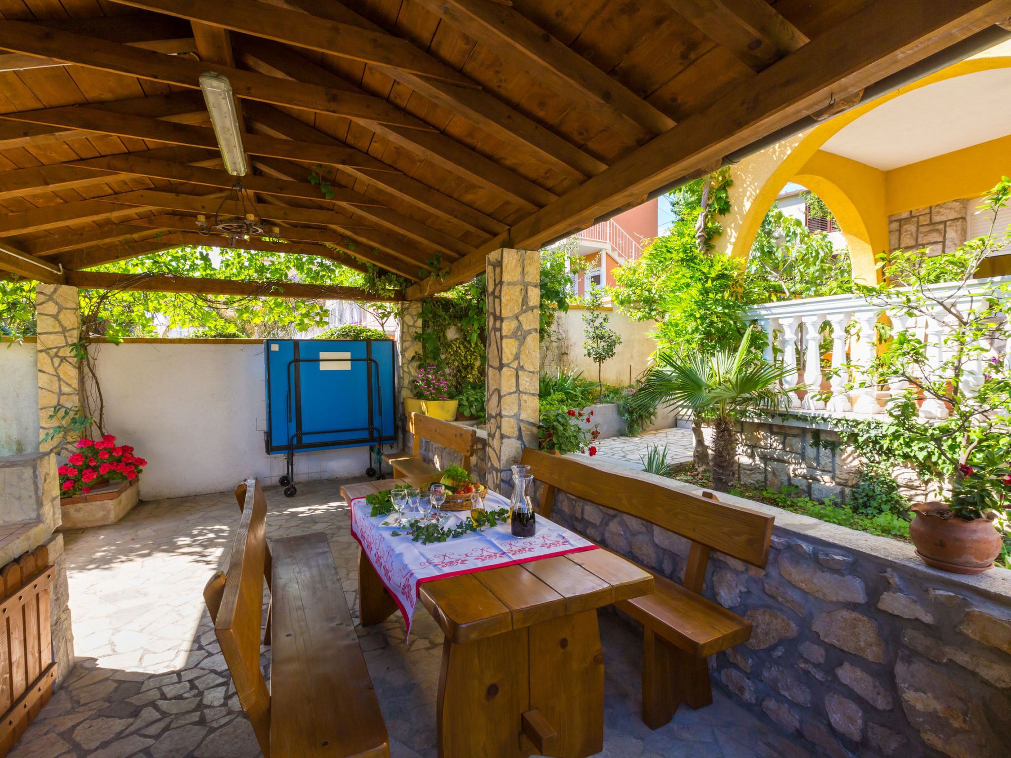 An outdoor patio with a wooden table set for dining, stone walls, and potted plants.