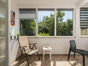 Ein Zimmer mit Fenster, Stuhl, kleinem Tisch und einem Topfpflanzen.