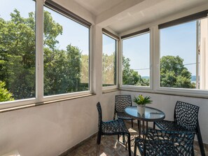 A sunlit room with a round table and chairs, large windows, and a view of trees and a body of water. - Palatino / HR-10637-01 by Interhome (Crikvenica)