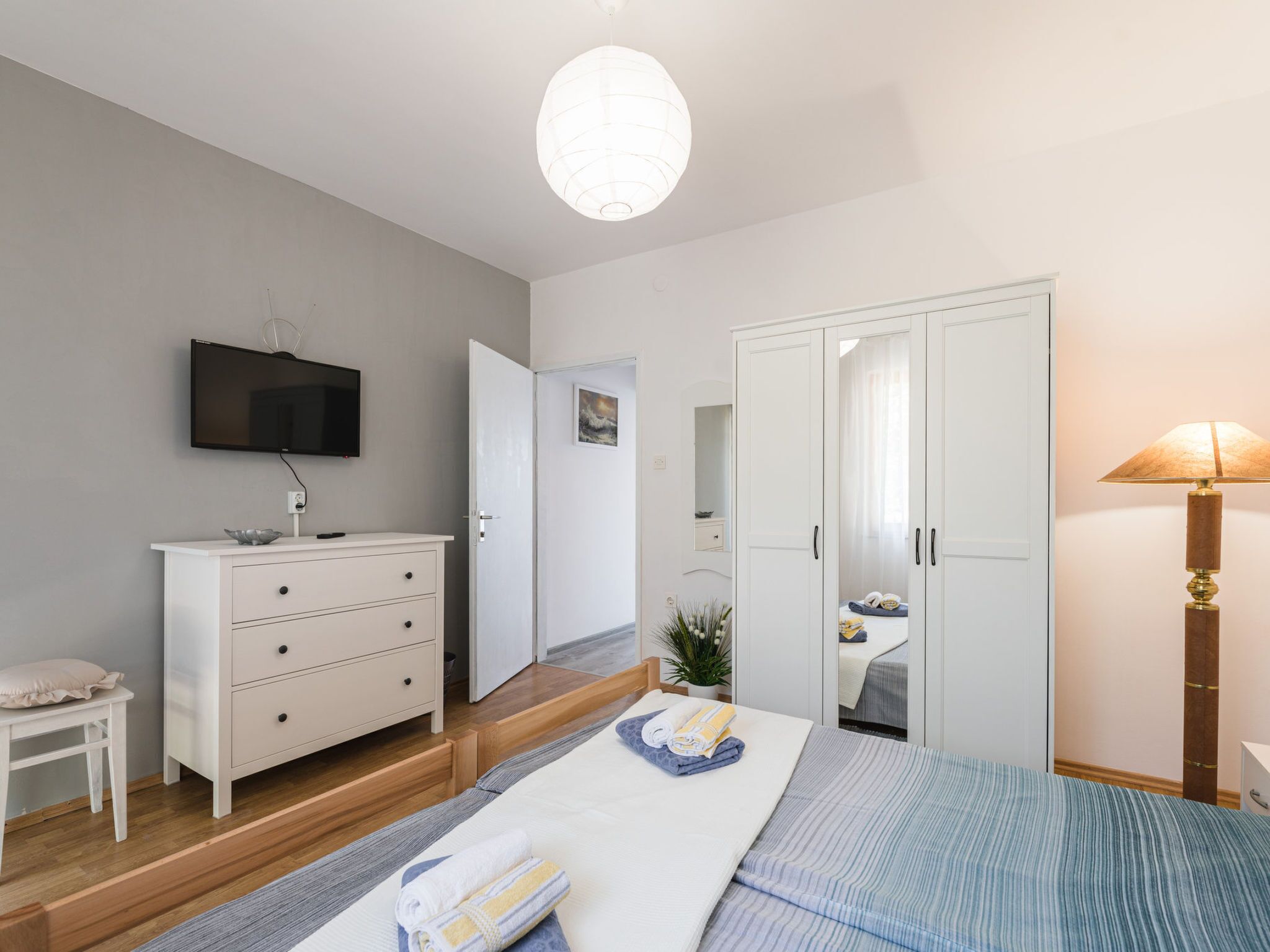 Ein modernes Schlafzimmer mit Bett, Nachttisch, Kommode, Fernseher, Kleiderschrank und Lampe.