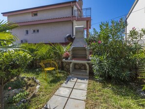 A garden with a stone bench, a yellow chair, and a stone structure. - VESNA / HR-08535-01 by Interhome (Crikvenica)