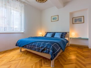 Ein Schlafzimmer mit einem Bett, zwei Nachttischen mit Lampen, einem Fenster mit Vorhängen und zwei gerahmten Bildern an der Wand.