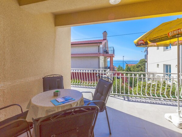 Ein Balkon mit Tisch und Stühlen, einem gelben Sonnenschirm und Blick auf Gebäude sowie das Meer.