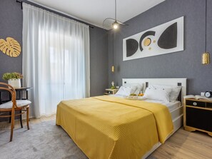 A modern bedroom with a large bed, a bedside table with a lamp, a chair, and a potted plant. - DIANA 2 / HR-02281-02 by Interhome (Crikvenica)