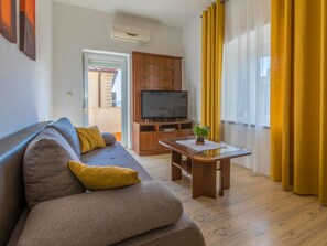 A living room with a sofa, a TV, a wooden cabinet, and a window with yellow curtains. - DIANA 2 / HR-02281-02 by Interhome (Crikvenica)