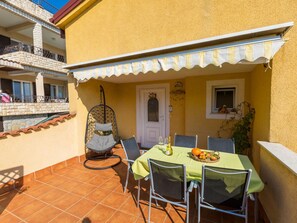 An outdoor patio with a table set for two, chairs, a hanging chair, and a small window with a plant. - DIANA 2 / HR-02281-02 by Interhome (Crikvenica)