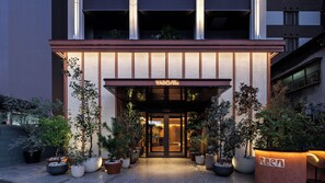 A hotel entrance with a modern design, featuring a large glass door, a welcoming awning, and a variety of potted plants. - YADO/Re YAKUIN (Fukuoka)