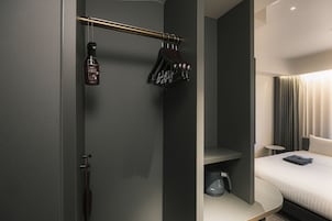 Habitación de hotel moderna con cama, mesita de noche, zona de ducha con perchero y un inodoro.