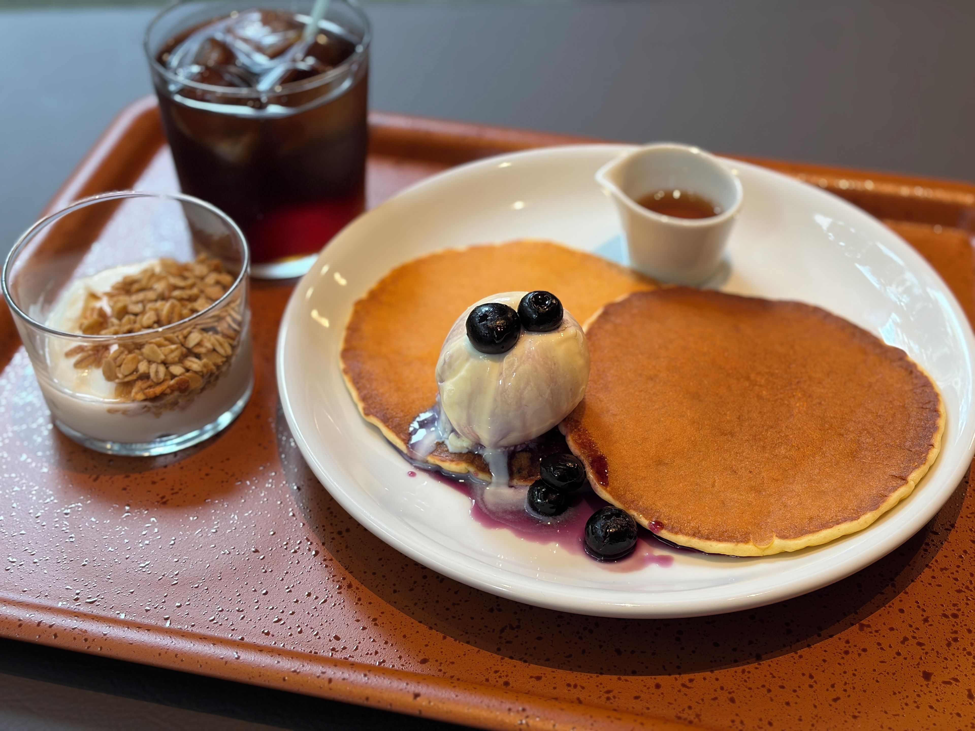 A breakfast plate with pancakes, blueberries, and a glass of milk with granola.