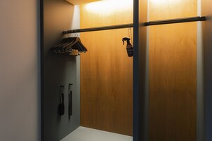 A room with a wooden wardrobe, a clothes rack with hangers, and a hanging spray bottle.