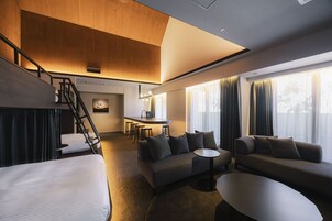 A modern hotel room with a staircase, a sofa set, a dining area, and large windows.