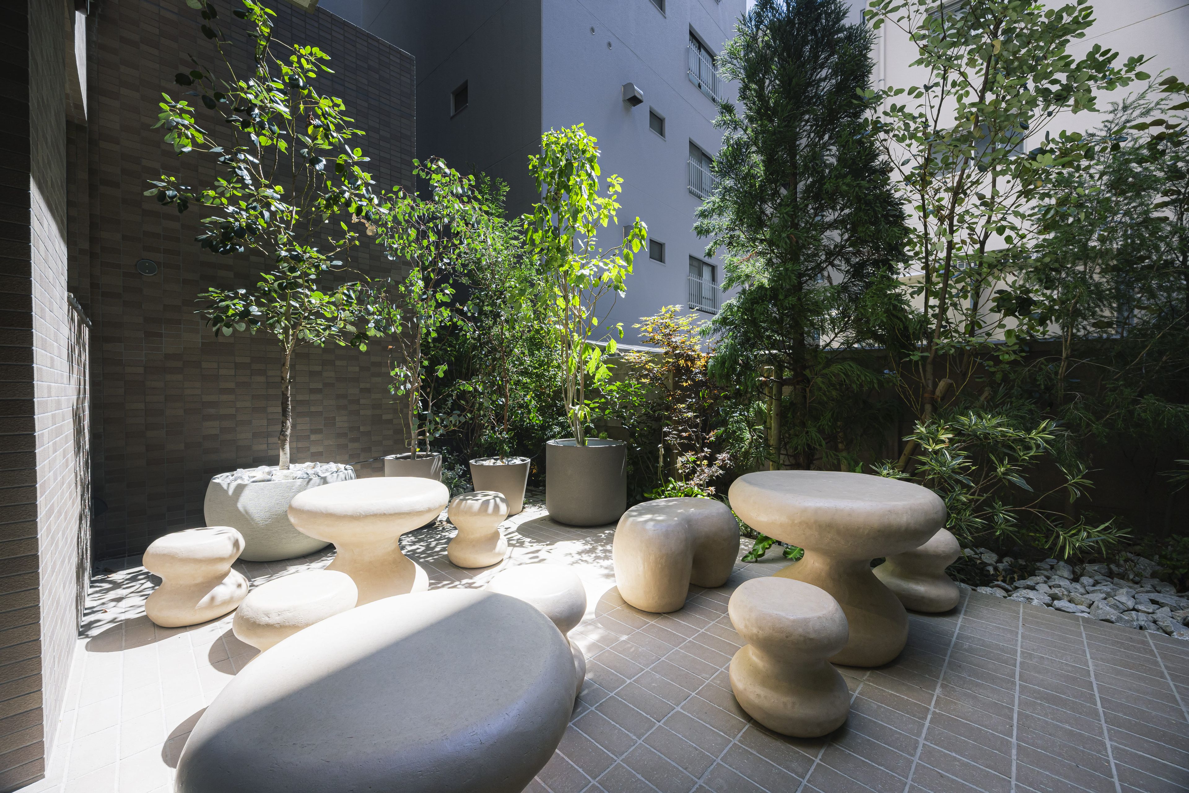 An outdoor seating area with stone tables and planters, surrounded by buildings and trees.
