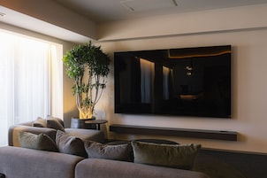 Una sala de estar moderna con un televisor de pantalla plana grande montado en la pared, un sofá gris con varios cojines y una planta en maceta.