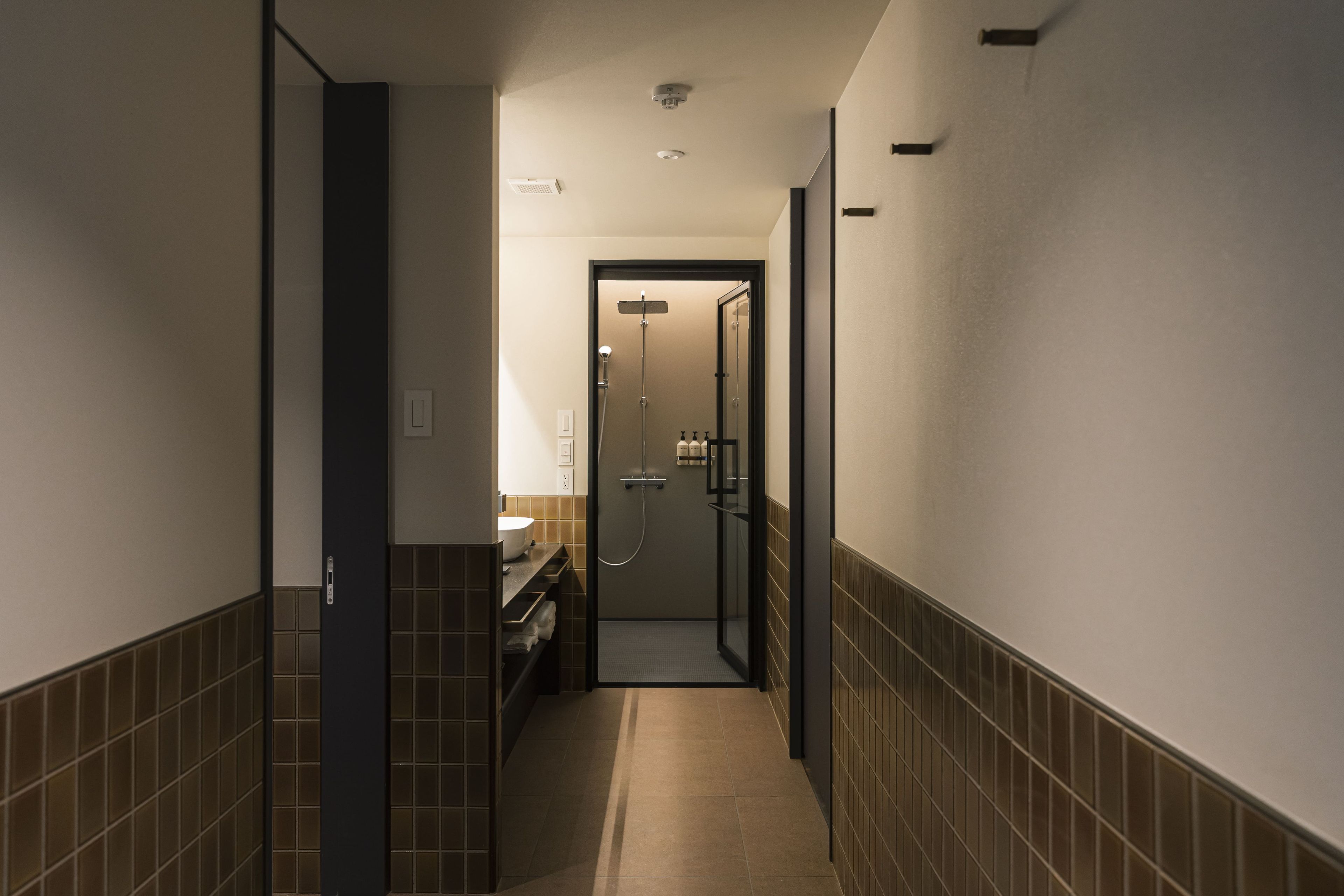 A narrow hallway with a bathroom at the end featuring a glass-enclosed shower and a toilet.