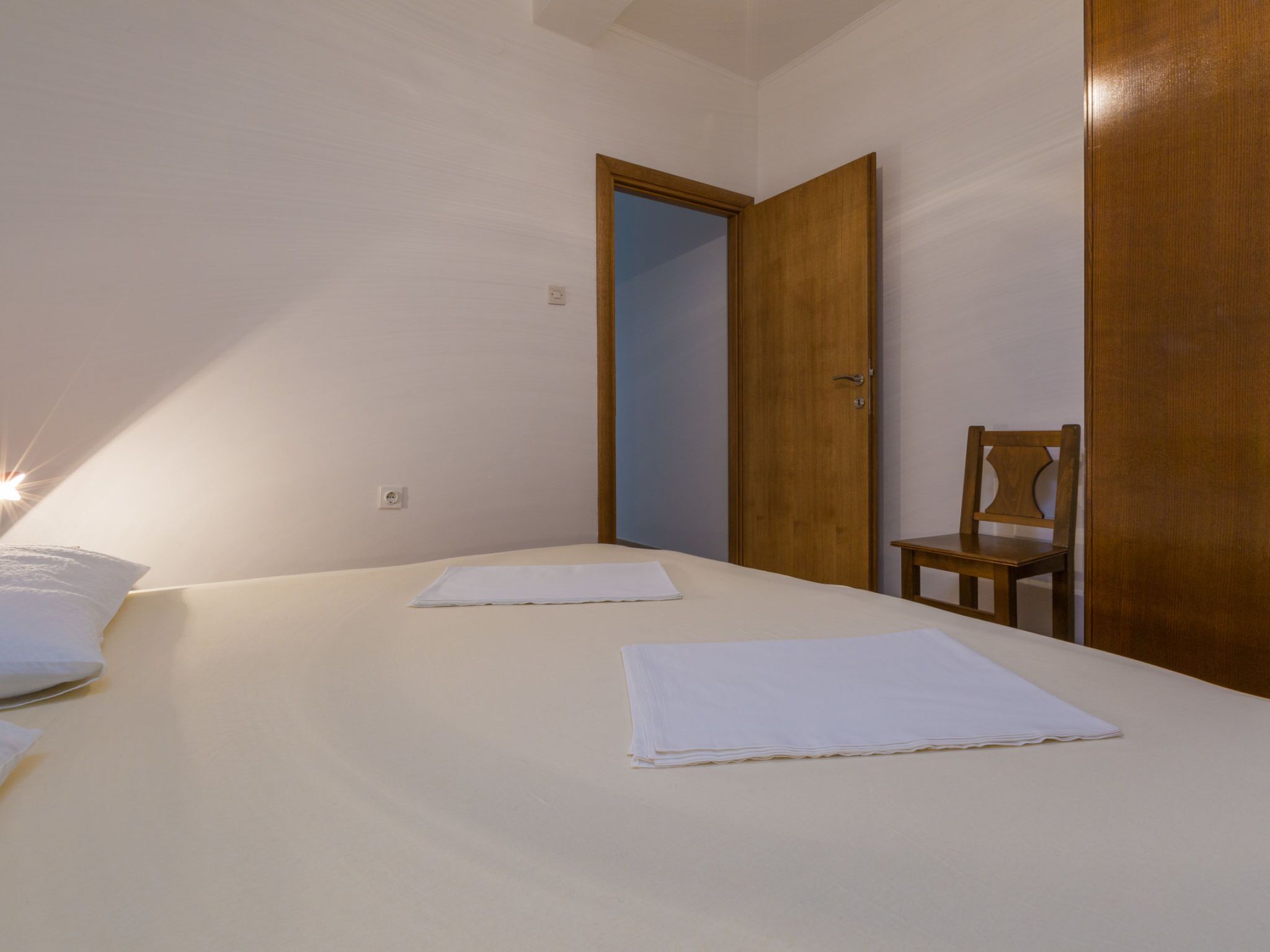 A bedroom with two beds, a wooden door, and a chair.