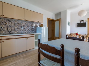 Eine kleine Küche mit gemustertem Fliesenspiegel, Holzschränken, einem weißen Kühlschrank und einem Essbereich mit Tisch und Stühlen.