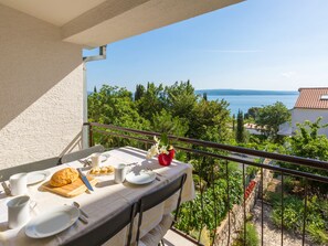 A balcony with a table set for breakfast overlooking a scenic view of trees and the sea. - IRIS 2 / HR-02362-02 by Interhome (Crikvenica)