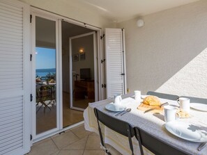 A dining area with a table set for two, a view of the sea through a sliding glass door, and a balcony with outdoor furniture. - IRIS 2 / HR-02362-02 by Interhome (Crikvenica)