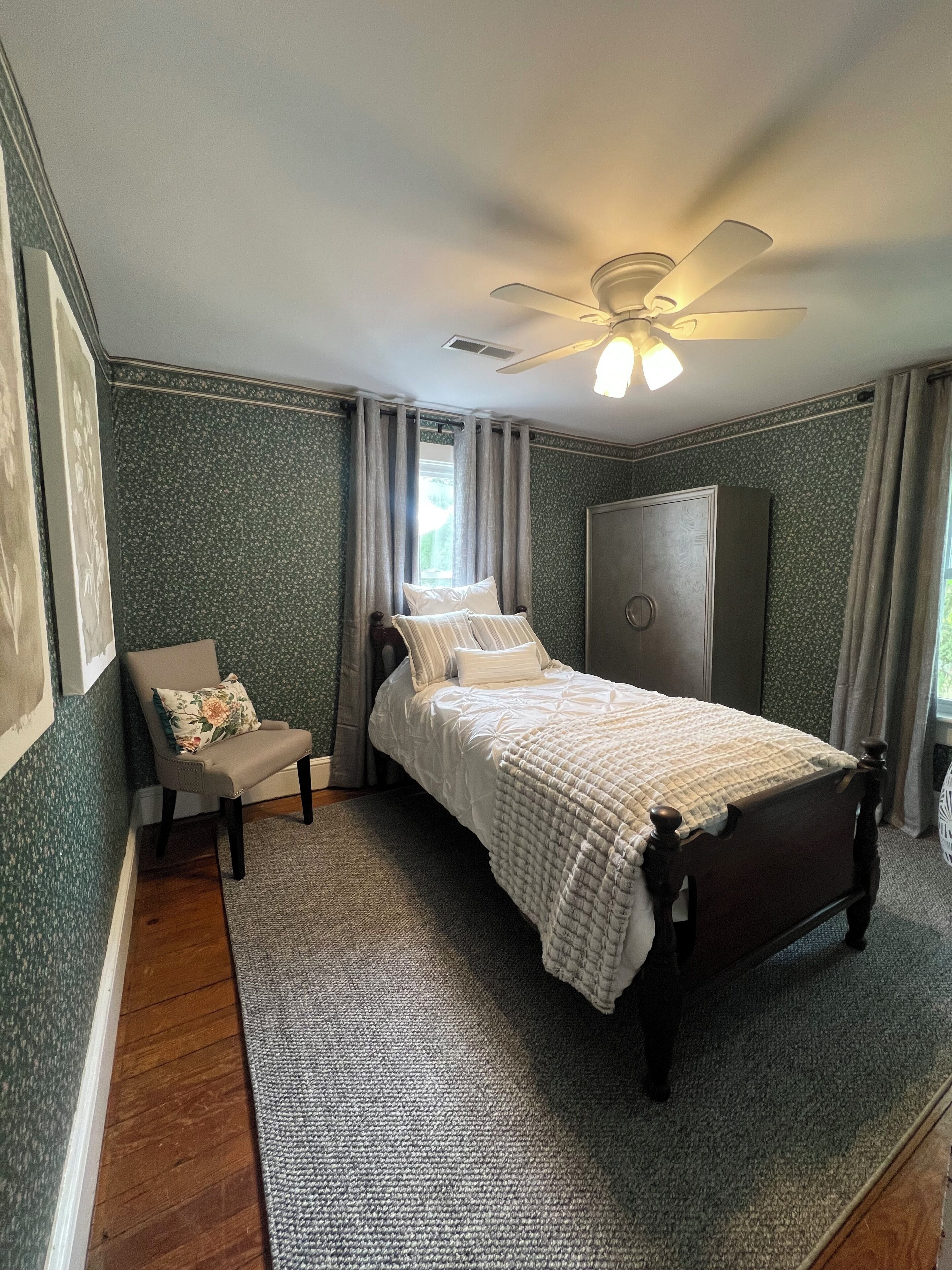 Une chambre à coucher comprenant un lit, une chaise, une armoire, un ventilateur de plafond et une fenêtre.