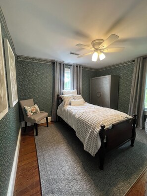Een slaapkamer met een bed, een stoel, een kledingkast, een plafondventilator en een raam.