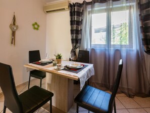 A dining area with a table set for two, chairs, a potted plant, and a window with curtains. - ANDREA 1 / HR-02612-01 by Interhome (Crikvenica)