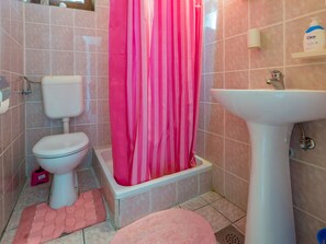 A bathroom with a toilet, a bathtub with a pink shower curtain, and a sink. - ANDREA 1 / HR-02612-01 by Interhome (Crikvenica)