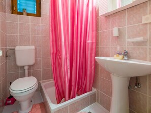 Ein Badezimmer mit Toilette, einer Badewanne, einem rosa Duschvorhang und einem Waschbecken mit Pflegeprodukten.