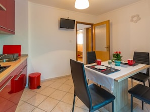 Une cuisine compacte avec un coin repas, un téléviseur fixé au mur et une porte donnant sur une autre pièce.