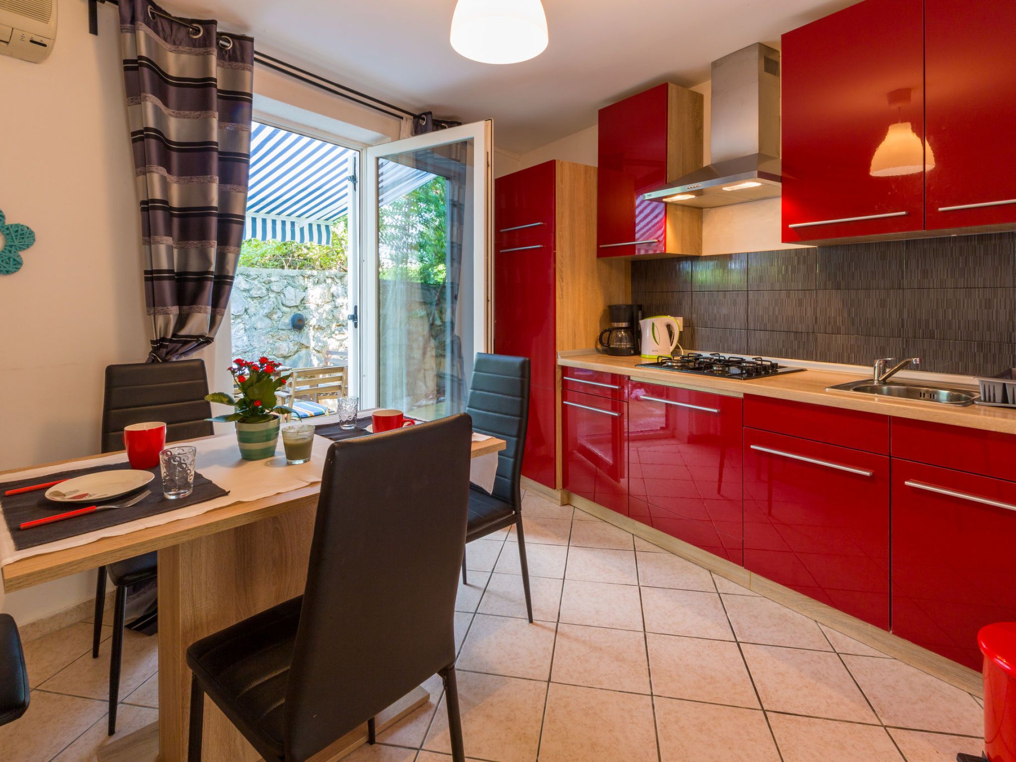 Een moderne keuken met rode kastjes, een gasfornuis en een eethoek met een tafel en stoelen.