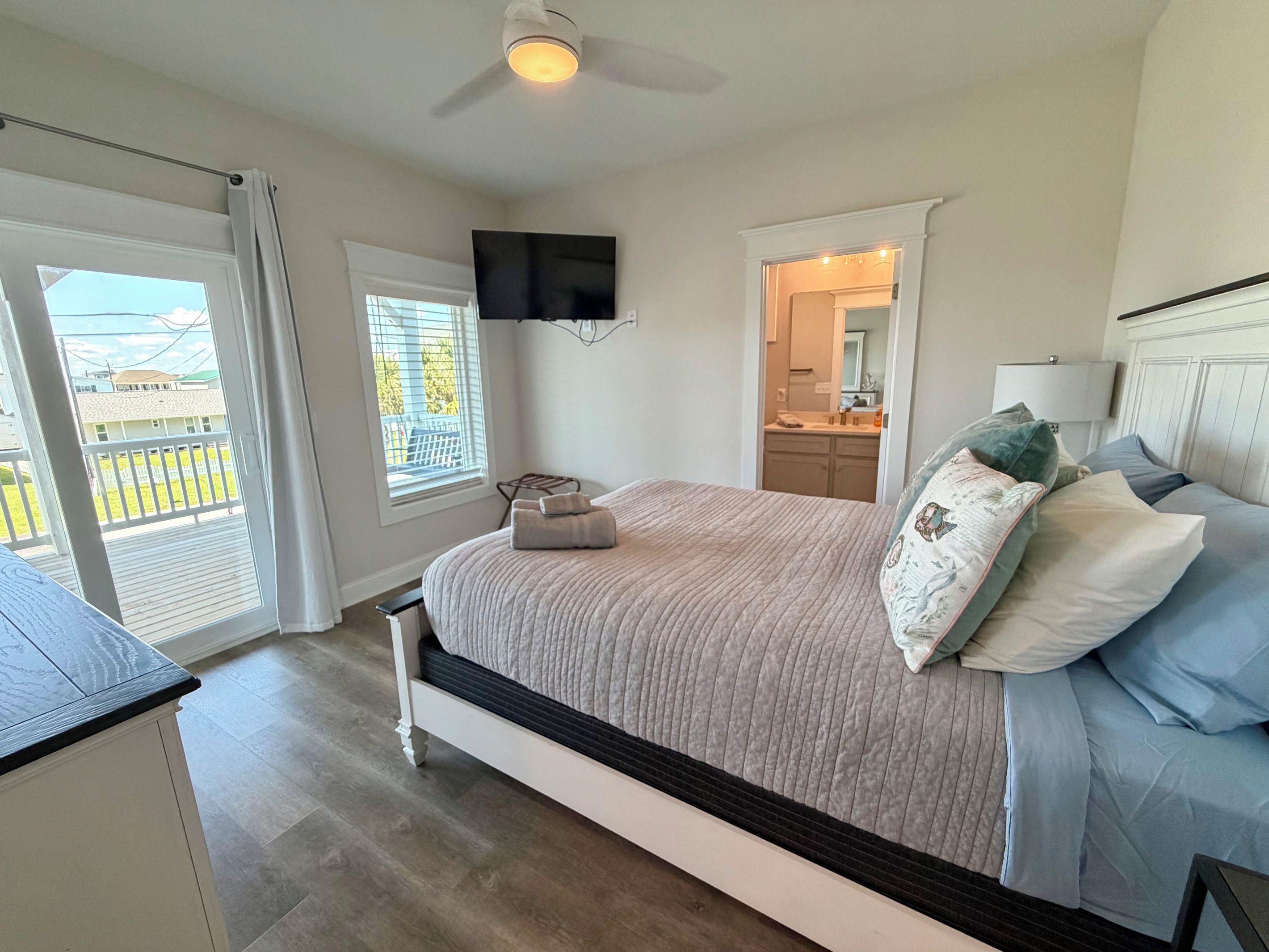 A bedroom with a bed, a ceiling fan, a TV mounted on the wall, and a view of the outside balcony.