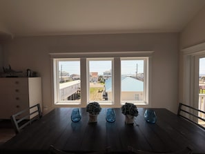 A dining area with a dark wooden table, three blue glass candle holders, and a view of a residential neighborhood through large windows. - Salty Breeze, 5 bed/4.5 bath POOL (Surf Cithh)