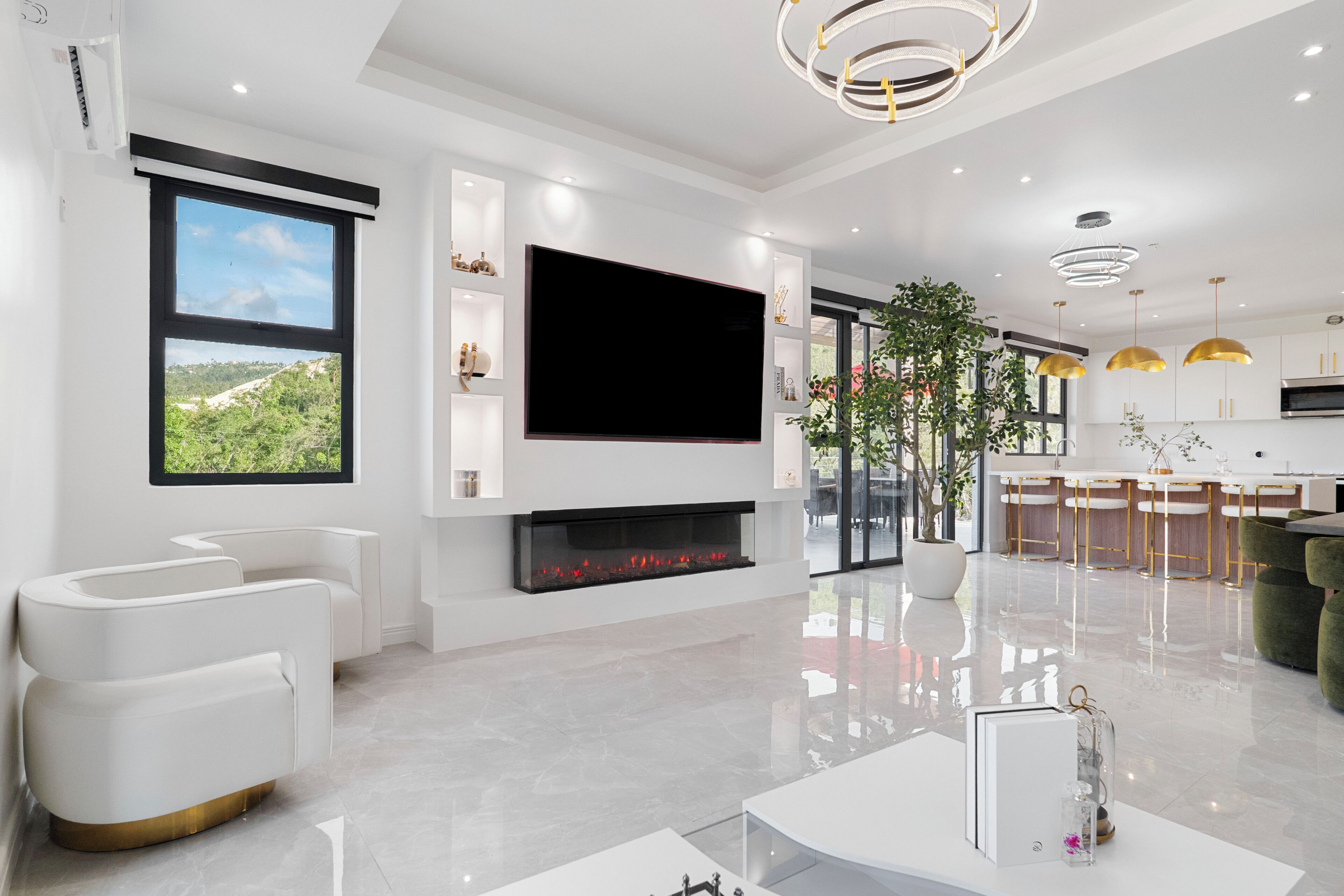 A modern living room with a flat-screen TV, a fireplace, and a large window overlooking a green landscape.