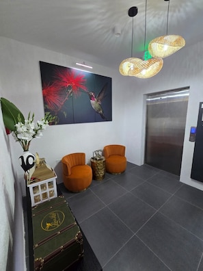 A lobby with a large painting of a hummingbird, two orange armchairs, a green trunk, and a modern light fixture. - Luxe Loft Penthouse, a luxury property in Montego Bay, 6 mins from MBJ airport (Montego Bay)