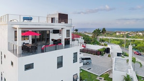 Um edifício moderno com terraço no telhado, área de estar ao ar livre e vista para o oceano.