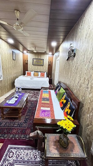 Una habitación con una cama, un sofá, una mesita de café, un jarrón decorativo y un ventilador de techo.