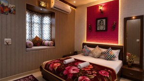 A hotel room with a large bed, a window with curtains, a wall-mounted air conditioner, and a red accent wall with a framed picture. - Hotel casa del sol (Jaisalmer)