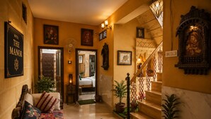 A hotel lobby with a sofa, a staircase, and a framed sign on the wall. - Hotel casa del sol (Jaisalmer)