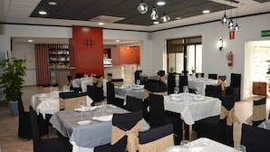 A restaurant with multiple tables set for dining, black chairs, and a red pillar. - Nuevo Hotel Capitolio (Valdepenas)