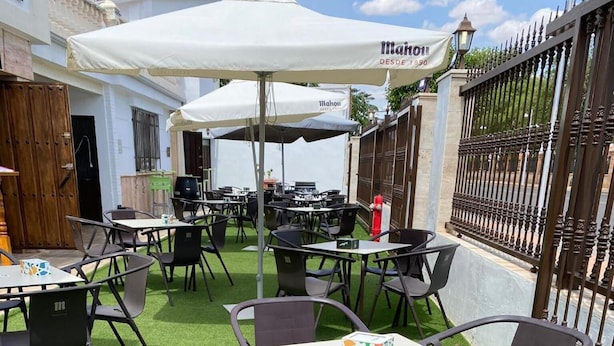 An outdoor seating area with tables and chairs, a white umbrella, and a fence. - Nuevo Hotel Capitolio (Valdepenas)