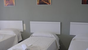 A hotel room with three single beds, each with a white bedspread and a towel. There are three framed pictures on the wall above the beds. - Nuevo Hotel Capitolio (Valdepenas)