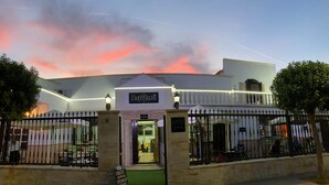 A building with a sign reading 'CAPITOLIO' at the entrance, a gated driveway, and a clear sky with clouds. - Nuevo Hotel Capitolio (Valdepenas)