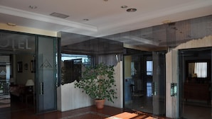 Een hotellobby met een grote potplant, betegelde vloer en glazen deuren die naar kamers leiden.