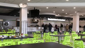 Een cafeteria met tafels en stoelen, een keukenhoek, en mensen aan het eten.