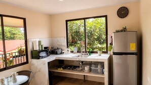 A compact kitchen with a built-in microwave, a refrigerator, and a sink. There is a window providing a view of greenery outside.