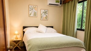 A neatly made bed with a green blanket, a bedside lamp, and an air conditioning unit on the wall.