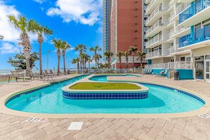 A pool area with multiple swimming pools, palm trees, and a tall building in the background. - Atlantica 452 Oceanfront Escape (Myrtle Beach)