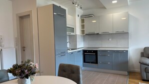 A modern kitchen with grey cabinets, a built-in oven, and a dining area with a white table and grey chairs. - Ados Apartment • Stunning Views • 3BR • Free Garage (Ilidža)