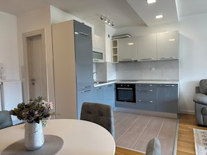 Una cocina moderna con armarios grises, horno empotrado y comedor con mesa blanca y sillas grises.