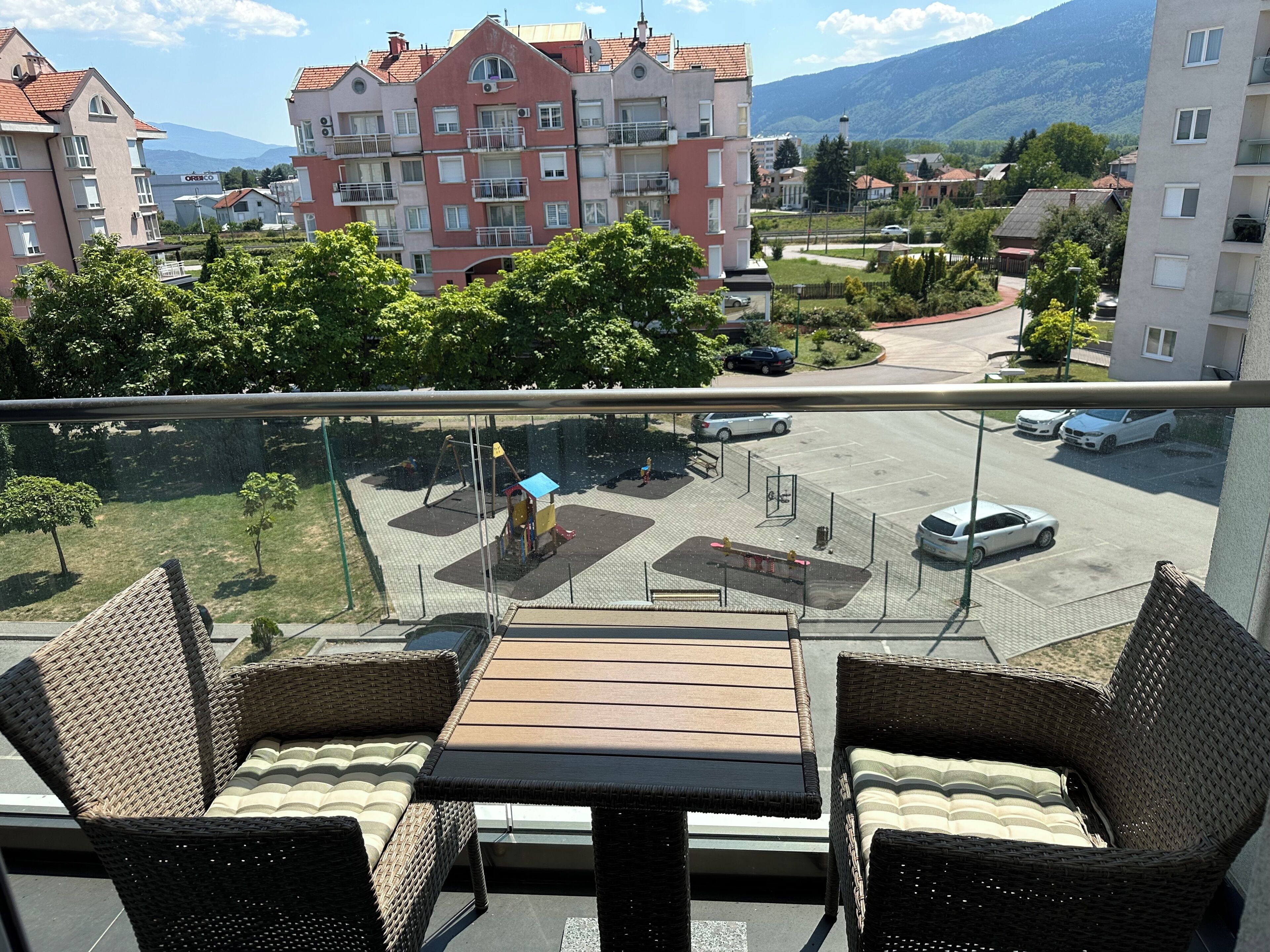 A balcony with wicker furniture overlooking a parking area and residential buildings.
